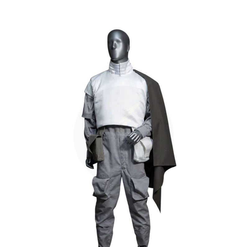 以下が含まれることがあります： マネキンの肩に黒いケープがかけられたグレーと白のコスチューム。コスチュームには、白いベスト、ポケット付きのグレーのパンツ、白いポーチが含まれています。マネキンは銀色の頭をしています。