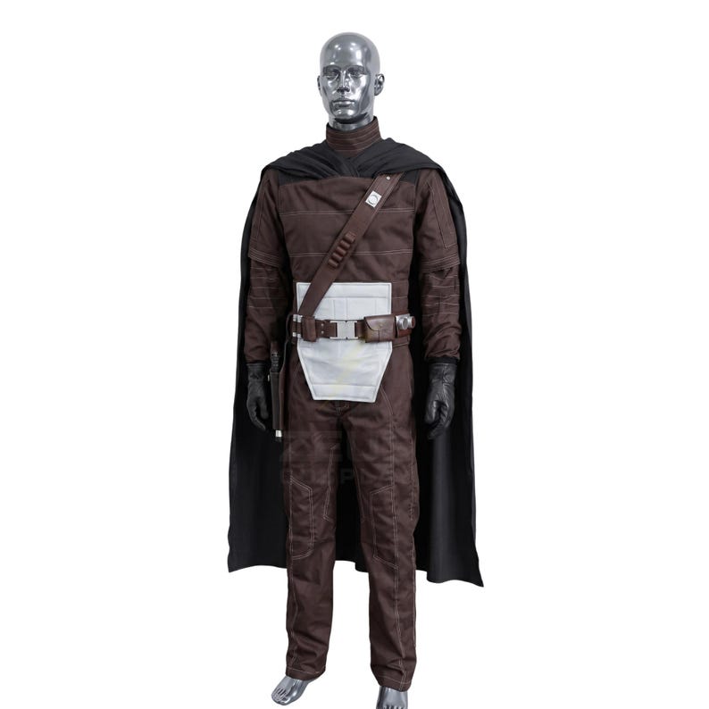 May include: A brown costume with a black cape, gloves, and a belt with a silver buckle. The costume includes a long-sleeved top, pants, and a white panel on the front. A mannequin displays the outfit.