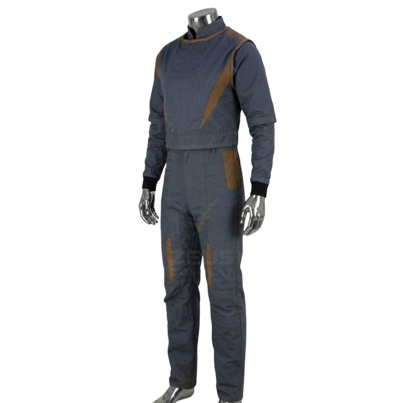 May include: A two-piece blue jumpsuit with brown accents. The top has a high collar and long sleeves, and the pants have brown patches on the knees. The sleeves have black cuffs. The outfit is displayed on a mannequin.