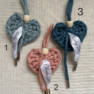 Peut inclure: Trois ornements en forme de cœur, crochetés, dans des tons de bleu et de rose. Chaque cœur est doté d'une boucle pour l'accrochage, d'une perle en bois et d'un ruban avec le texte "Clody '26". Les cordons ont des embouts métalliques.