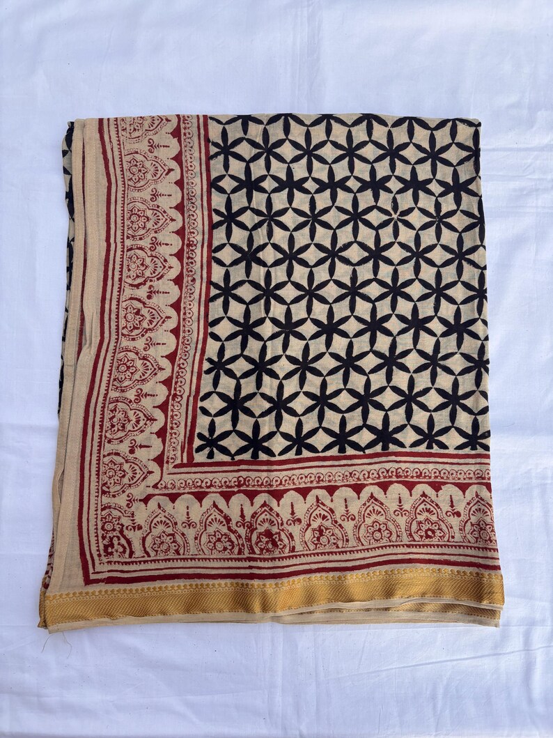 May include: A rectangular textile featuring a beige base with a black geometric floral pattern across the main body. The border displays a dark red intricate paisley-style print, finished with a solid gold-toned band along the bottom edge.