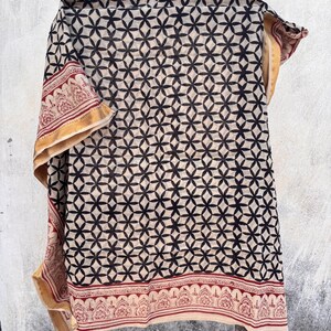 May include: A rectangular textile featuring a repeating black geometric floral pattern on a cream background. The fabric has a wide border with a red and cream intricate paisley-style design and a solid gold-toned edge along the vertical sides.