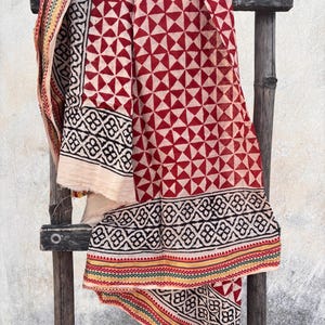 May include: A rectangular textile featuring a repeating pattern of red triangles on a cream background. The fabric includes a wide black border with a geometric floral motif and a thin edge strip with alternating green, yellow, and red lines.