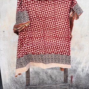 May include: A rectangular textile featuring a repeating pattern of red and cream triangles across the main body. The fabric includes a wide black and cream geometric border along the bottom edge, with additional patterned trim on the side edges.