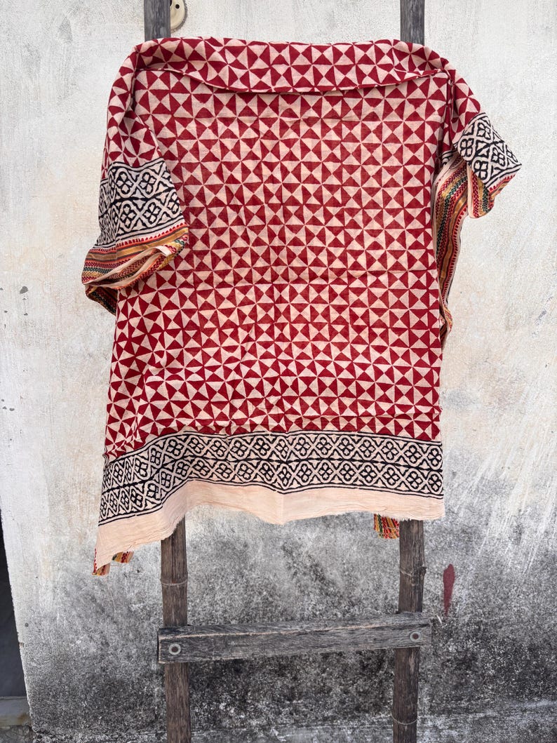 May include: A rectangular textile featuring a repeating pattern of red and cream triangles across the main body. The fabric includes a wide black and cream geometric border along the bottom edge, with additional patterned trim on the side edges.