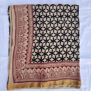 May include: A rectangular textile featuring a cream-colored base with a repeating black geometric floral pattern. The border displays a deep red intricate botanical print, finished with a solid gold-toned band along the bottom edge.