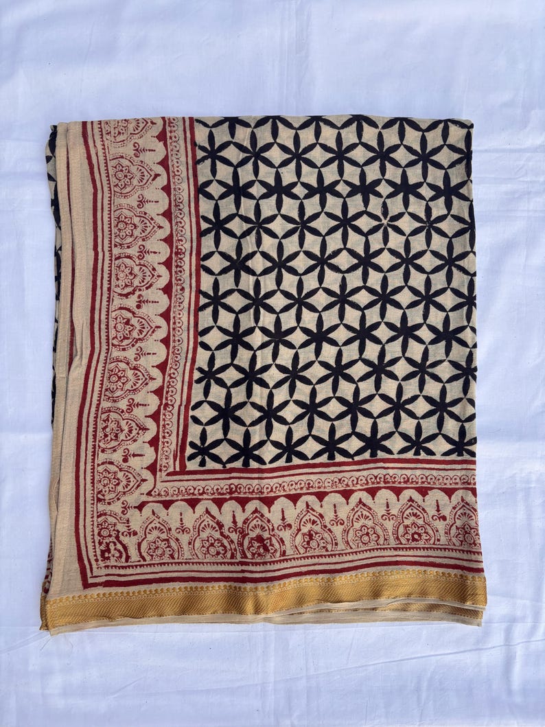 May include: A rectangular textile featuring a cream-colored base with a repeating black geometric floral pattern. The border displays a deep red intricate botanical print, finished with a solid gold-toned band along the bottom edge.