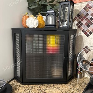 May include: A black corner cabinet with a ribbed glass door, topped with decorative pumpkins and lanterns. The cabinet is in a kitchen setting, with the text "XCraftsCo" visible on the side.