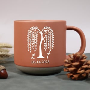 May include: A terracotta-coloured ceramic mug with a white weeping willow tree design. The mug features the initials "L T" and the date "03.14.2025" in white. The mug has a brown handle and a grey base.