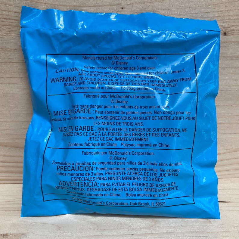 May include: A blue plastic bag with printed text in multiple languages. The bag is from McDonald's and has warnings about small parts and suffocation hazards. The bag is sealed and appears to be new.