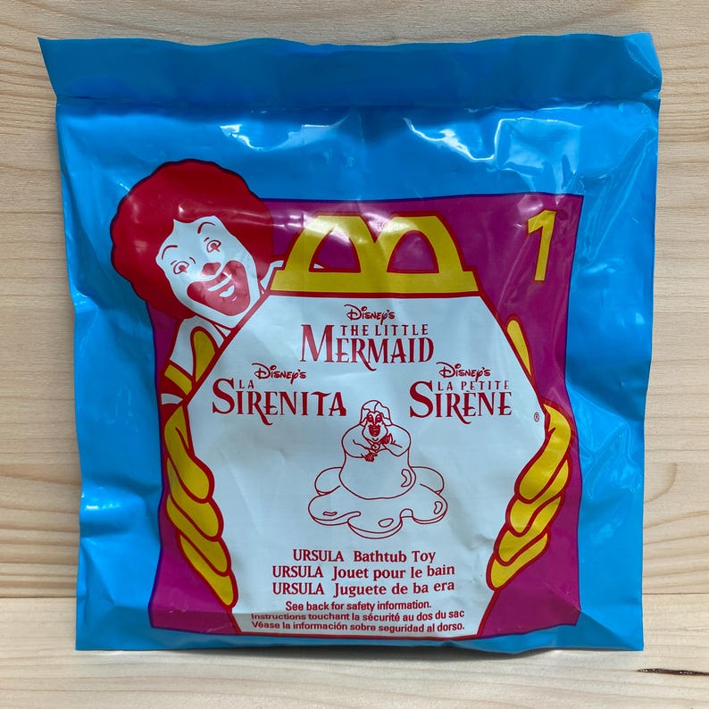May include: A sealed blue plastic bag with a pink and white graphic. The graphic includes the McDonald's logo, the text "Disney's The Little Mermaid", and an illustration of Ursula. The bag also has the number "1" and text in multiple languages.