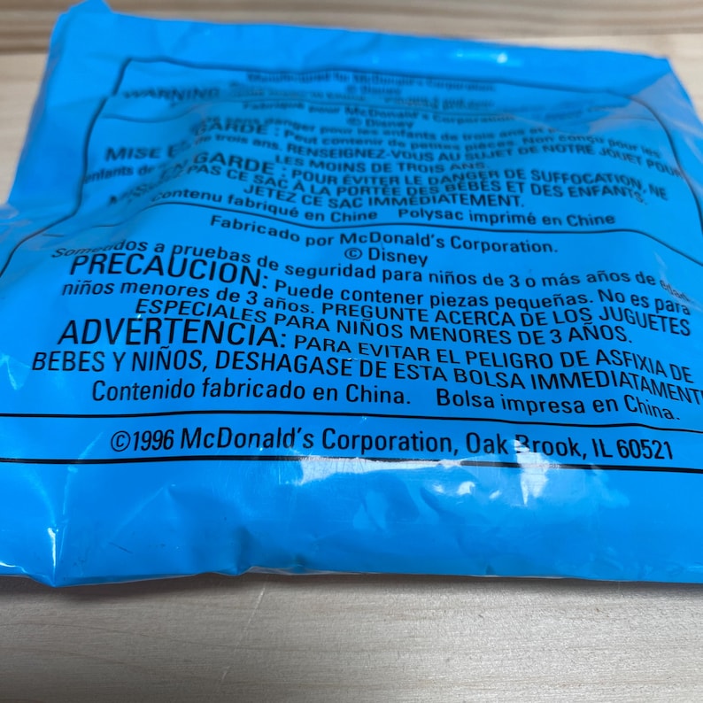 May include: A close-up of a blue plastic bag with printed text in multiple languages. The text includes warnings and safety information. The bag is from McDonald's Corporation, Oak Brook, IL 60521.