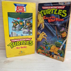 May include: Two VHS tapes featuring Teenage Mutant Ninja Turtles. One is yellow with the Burger King Kids Club logo and "Sky Turtles" text. The other tape is black with "Case of the Killer Pizzas" text.