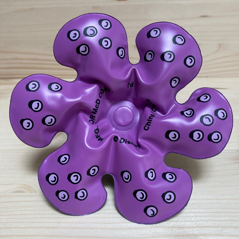 May include: A purple, flower-shaped toy with black and white circular designs. The toy has a central circular feature and text that reads "&copy; Disney" and "China/C".