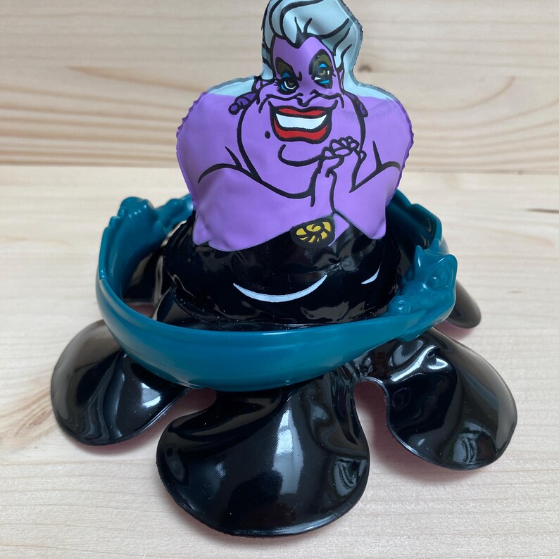 May include: A colourful Ursula figurine from The Little Mermaid. The figurine features a purple face with a sinister smile, a black body, and a teal-coloured base. The base has a shell-like design.