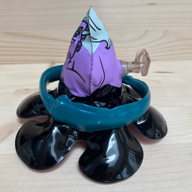 May include: A black, flower-shaped toy with a teal ring and a purple and white fabric cone. The cone features a cartoon character design. A clear plastic piece extends from the side of the cone.