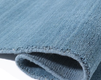 May include: Close-up of a rolled-up, light blue rug. The rug has a soft, textured surface with a visible pile. The edges are neatly finished, and the overall appearance suggests a comfortable and inviting home decor item.