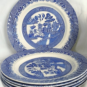 Może przedstawiać: Stos niebiesko-białych ceramicznych talerzy z klasycznym wzorem Willow. Talerze mają centralną scenę krajobrazową otoczoną szczegółową obwódką. Talerze są ułożone jeden na drugim.