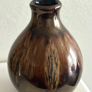 Könnte beinhalten: Eine kleine, braune Keramikvase mit glänzendem Finish. Die Vase hat einen abgerundeten Körper und einen schmalen Hals. Die Glasur hat einen Marmoreffekt mit dunkelbraunen und schwarzen Streifen. Die Vase ist etwa 15 cm hoch.