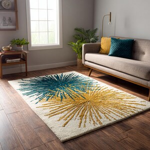 May include: A rectangular area rug featuring a cream-colored background with two large, textured starburst patterns in teal and mustard yellow. The design consists of radiating lines extending from a central point, creating a high-contrast visual effect.