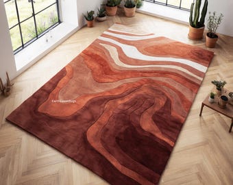 May include: A rectangular area rug with a layered design in shades of brown, rust, and cream. The rug's pattern resembles contour lines, creating a textured, earthy aesthetic. The rug is placed on a wooden floor, and the brand name "EarthLoomRugs" is visible.