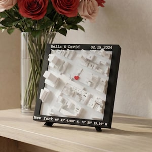 Può includere: Una mappa 3D con cornice nera di New York City con un cuore rosso che segna una posizione. La mappa include il testo "Bella & David" e "02.19.2024". Un bouquet di rose rosse e rosa è in un vaso trasparente.