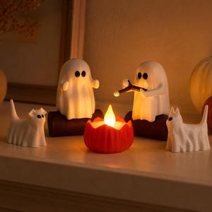 Peut inclure: Deux figurines de fantômes blancs sont assises sur des bûches marron foncé, l'une tenant un bâton au-dessus d'une bougie LED orange en forme de citrouille. Deux figurines de chats fantômes blancs se tiennent de chaque côté.