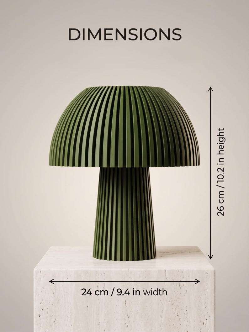 Puede incluir: Una l&aacute;mpara de mesa de color verde oliva oscuro con una pantalla en forma de seta y una base cil&iacute;ndrica, ambas con listones verticales. El texto DIMENSIONS aparece en la parte superior. La l&aacute;mpara mide 26 cm de alto y 24 cm de ancho.