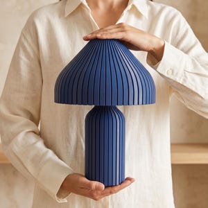 May include: A dark blue table lamp featuring a mushroom-shaped shade and a cylindrical base, both characterized by a series of vertical, evenly spaced ridges that create a textured, ribbed appearance across the entire surface of the lamp.