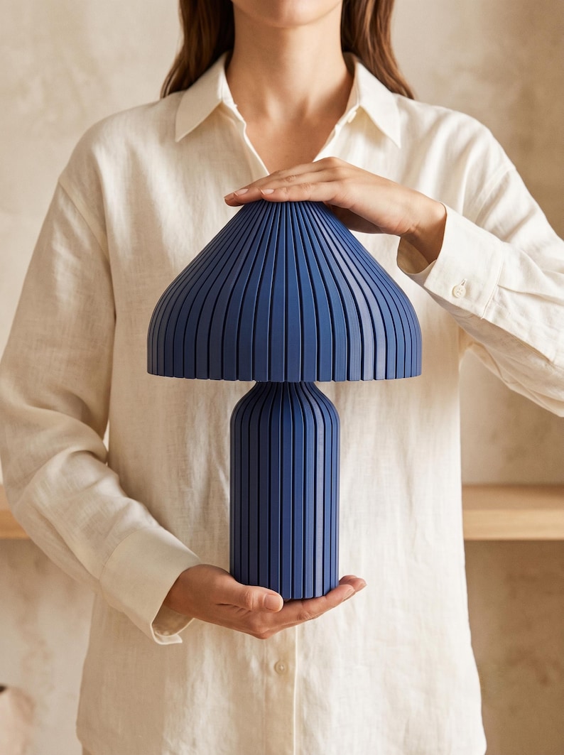 May include: A dark blue table lamp featuring a mushroom-shaped shade and a cylindrical base, both characterized by a series of vertical, evenly spaced ridges that create a textured, ribbed appearance across the entire surface of the lamp.