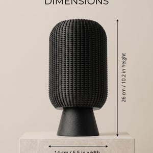 K&ouml;nnte beinhalten: Eine schwarze Vase mit einer texturierten, gitterartigen Oberfl&auml;che und einem glatten, konischen Fu&szlig;. Das Objekt ist mit Ma&szlig;en von 26 cm H&ouml;he und 14 cm Breite versehen. Der Text DIMENSIONS steht oben im Bild.