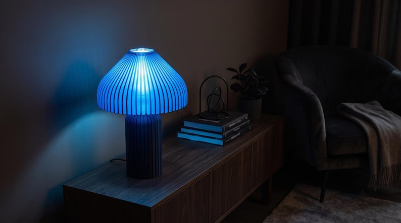 May include: A table lamp with a cylindrical base and a wide, mushroom-shaped shade, both featuring a vertical ribbed texture. The lamp emits a bright, vibrant blue light that illuminates the surrounding area with a distinct glow.