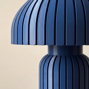 May include: A dark blue table lamp featuring a mushroom-shaped shade and a cylindrical base, both constructed with vertical slats. The lamp has a smooth, matte finish and a uniform deep navy color throughout its entire structural design.