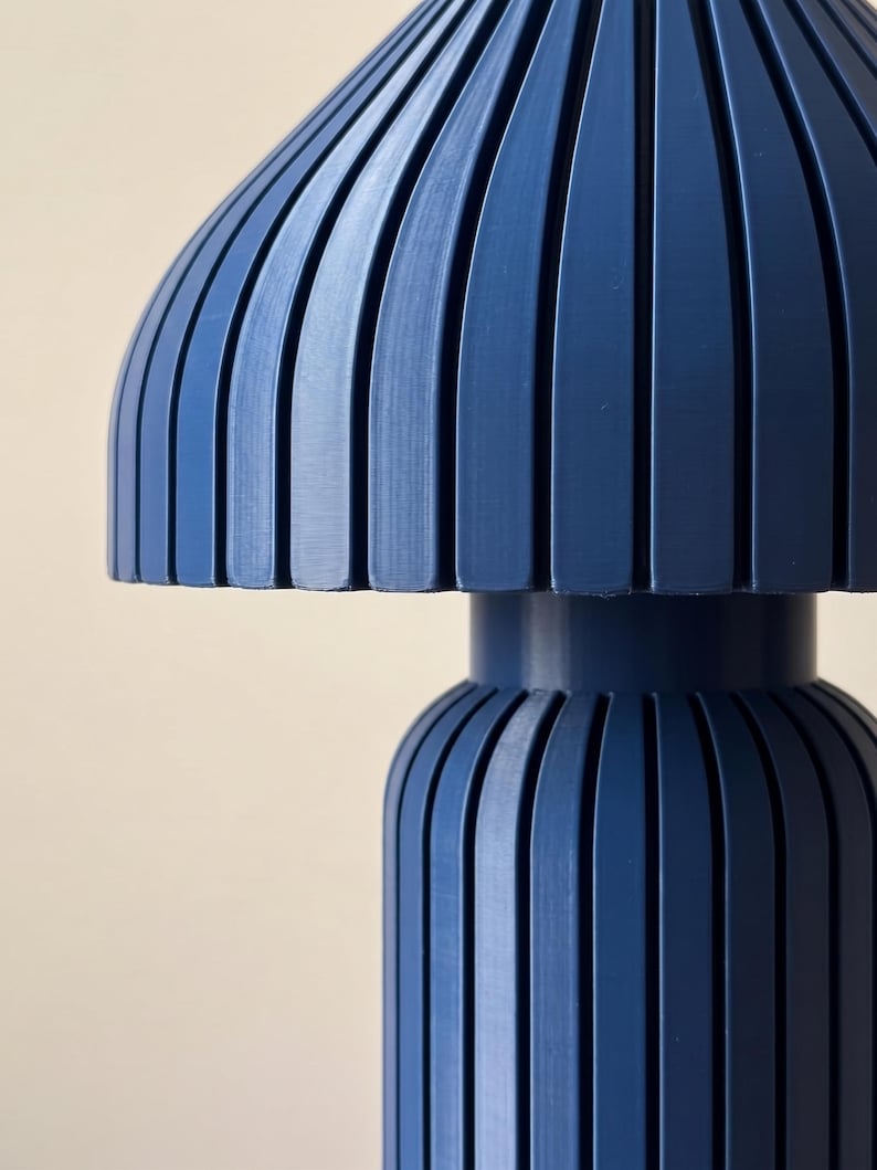 May include: A dark blue table lamp featuring a mushroom-shaped shade and a cylindrical base, both constructed with vertical slats. The lamp has a smooth, matte finish and a uniform deep navy color throughout its entire structural design.