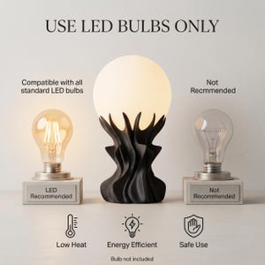 May include: A black sculptural table lamp with a frosted globe shade. The lamp is flanked by two light bulbs, one LED and one incandescent, with text indicating LED bulbs are recommended. The image includes text: "USE LED BULBS ONLY".