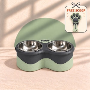 Puede incluir: Una estación doble de cuencos para mascotas con dos insertos de acero inoxidable sobre una base gris oscuro y verde salvia. El centro presenta la palabra BUDDY. Un gráfico muestra una pala con forma de pata verde salvia con el texto FREE SCOOP y BOODY.