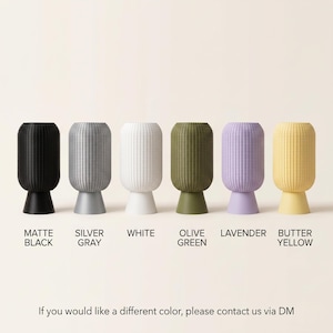 K&ouml;nnte beinhalten: Sechs zylindrische, texturierte Vasen auf Sockeln in Mattschwarz, Silbergrau, Wei&szlig;, Olivgr&uuml;n, Lavendel und Buttergelb. Der Text unter jeder Vase lautet: MATTE BLACK, SILVER GRAY, WHITE, OLIVE GREEN, LAVENDER, BUTTER YELLOW. Text unten: If you would like a different color, please contact us via DM.