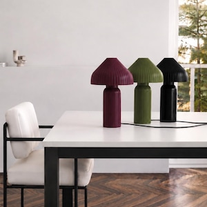 May include: Three table lamps with a mushroom-shaped silhouette and a vertical ribbed texture. The lamps are colored in deep burgundy, olive green, and black, each featuring a cylindrical base and a wide, flared shade with a black power cord.