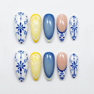 May include: A set of ten artificial nails in various designs. The designs include white nails with blue floral patterns, yellow lemon slice nails, blue ombre nails, and pink nails with blue floral tips.