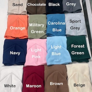 May include: A collection of fleece neck gaiters in various colors, including sand, chocolate, black, grey, orange, military green, Carolina blue, sport grey, navy, light pink, light blue, forest green, white, maroon, brown, and beige. Each gaiter is folded and labeled with its color.