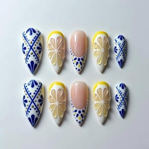 May include: A set of ten almond-shaped press-on nails. Designs include white nails with blue and gold patterns, lemon slice accents, and a pink French tip with blue and yellow polka dots. The nails are arranged on a white surface.