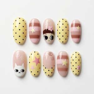 May include: A set of ten artificial nails with various designs. The nails feature yellow with black polka dots, pink and brown stripes, cartoon faces, and star and swirl patterns. The nails are oval-shaped.