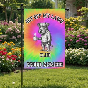 May include: A colorful garden flag with the text "GET OFF MY LAWN CLUB PROUD MEMBER." The flag features a cartoon dog holding a mug, set against a tie-dye background of orange, purple, green, and blue. The flag is displayed in a garden.