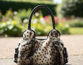May include: A handbag with a spotted pattern in black and cream, featuring black leather accents and handles. The bag has a structured shape with decorative silver-toned hardware and a soft, textured appearance.
