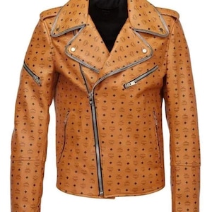 Könnte beinhalten: Hellbraune Leder-Motorradjacke mit schwarzem Innenfutter. Die Jacke hat einen silbernen Reißverschluss, mehrere Taschen und ein sich wiederholendes Muster aus schwarzen Rauten. Klassisches asymmetrisches Design.