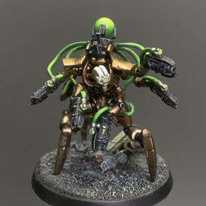 May include: A detailed miniature figure of a robotic warrior with a green and gold color scheme. The figure has multiple arms, weapons, and green tubing. It is mounted on a textured, circular base.