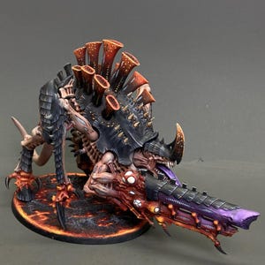 Può includere: Figura in miniatura dettagliata di una creatura Tirannide, con una tavolozza di colori nero, viola, rosso e beige. Il modello presenta una grande arma a più canne e una base strutturata, che mostra dettagli intricati e un design minaccioso.