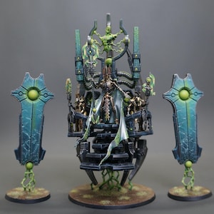 May include: A detailed miniature model of a throne with a skeletal figure and several smaller figures. The throne is dark gray with green accents, and the skeletal figure is wearing a white and green cloak. Two teal and green shield-like structures flank the throne.