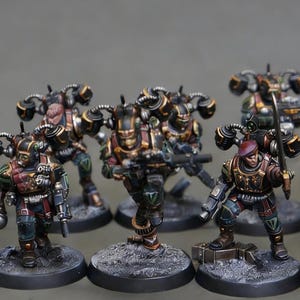 May include: A collection of miniature figurines, each depicting a soldier in detailed armor. The figures are painted in shades of brown, gold, and green, with intricate detailing on their weapons and gear. They stand on circular bases.