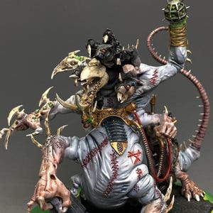 May include: A painted miniature figure of a multi-limbed creature with pale blue skin, featuring visible red stitched scars, a large bone-like head structure, and several small black rat-like creatures perched on its back, holding a metal cage.